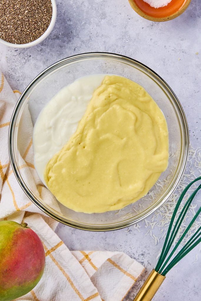 Greek yogurt added to mango mixture in a glass bowl