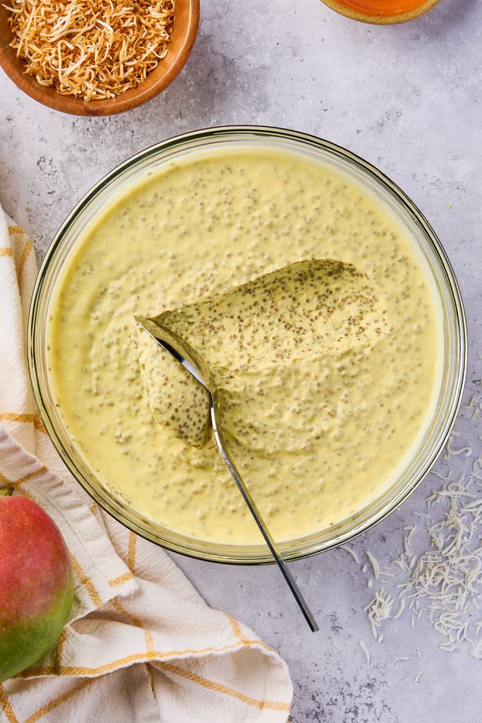 mango chia pudding in a glass bowl with a spoon scooping the pudding