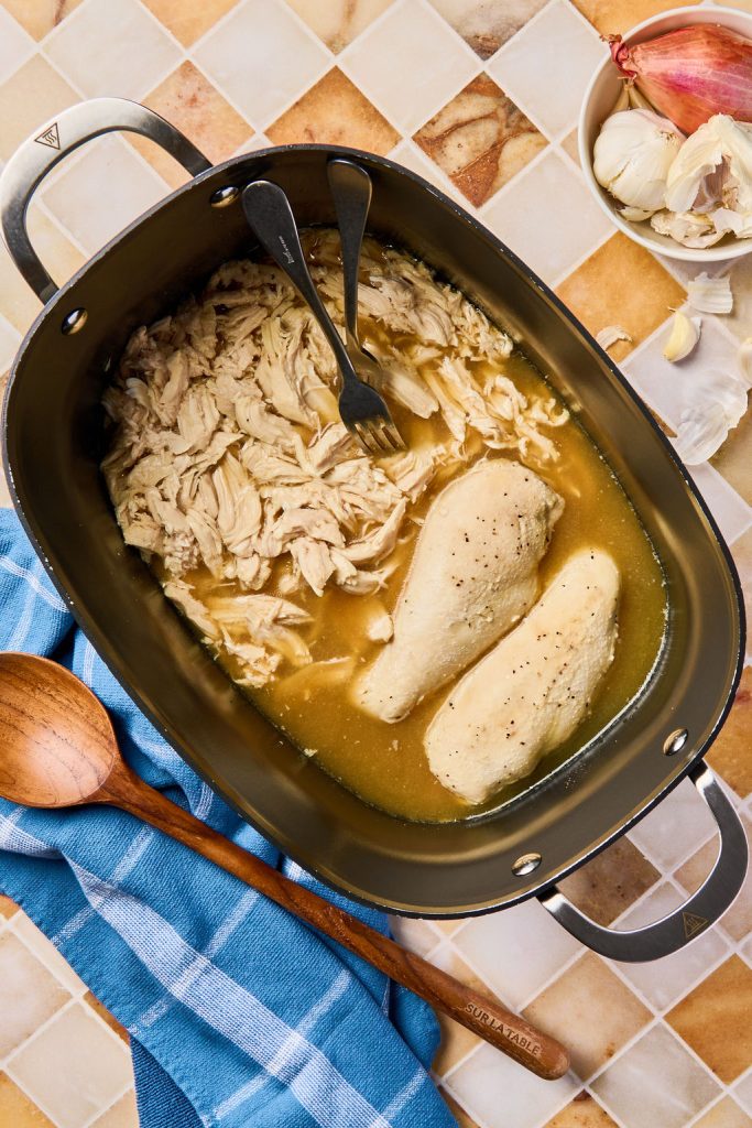 cooked chicken being shredded by two forks in the crockpot