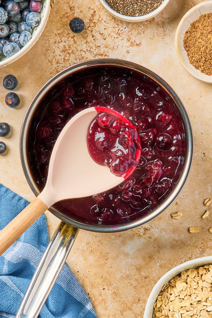 blueberries cooked down in a sauce pan with a wooden spoon showing close up
