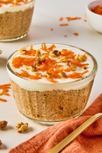 carrot cake chis pudding in a glass serving container topped with Greek yogurt, shredded carrots and nuts