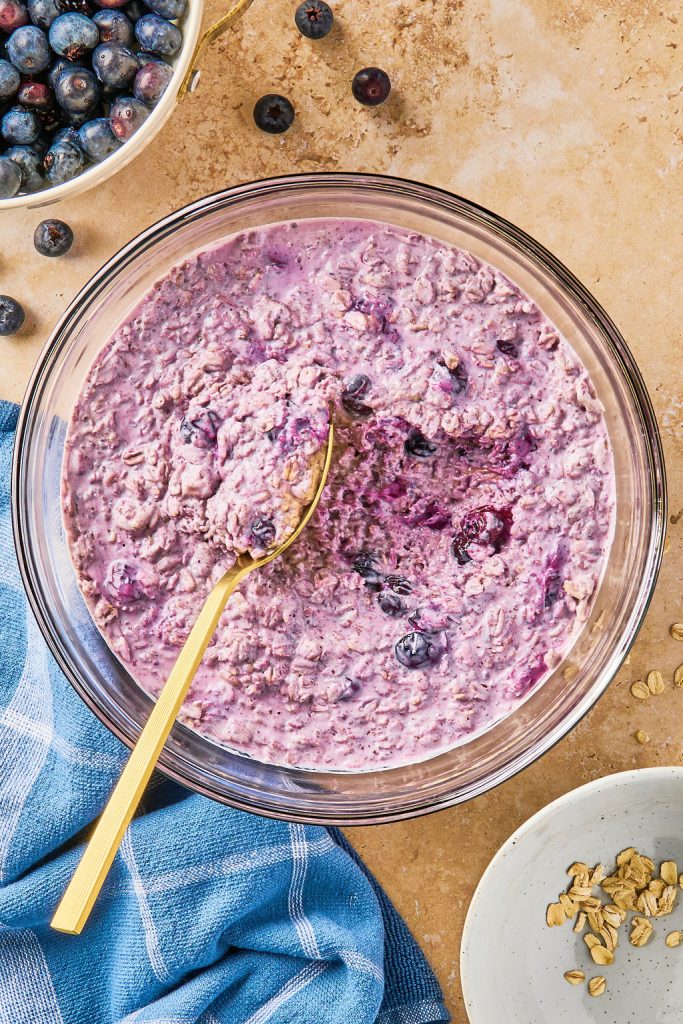 refrigerated blueberry oats being scooped by a golf spoon in a glass bowl
