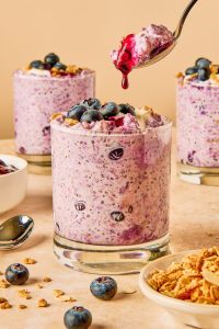 blueberry compote dripping off a golden spoon into a glass of blueberry overnight oats