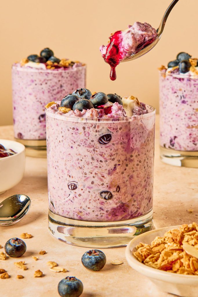 A glass jar with blueberry overnight oats and a spoon with a drip of blueberry sauce