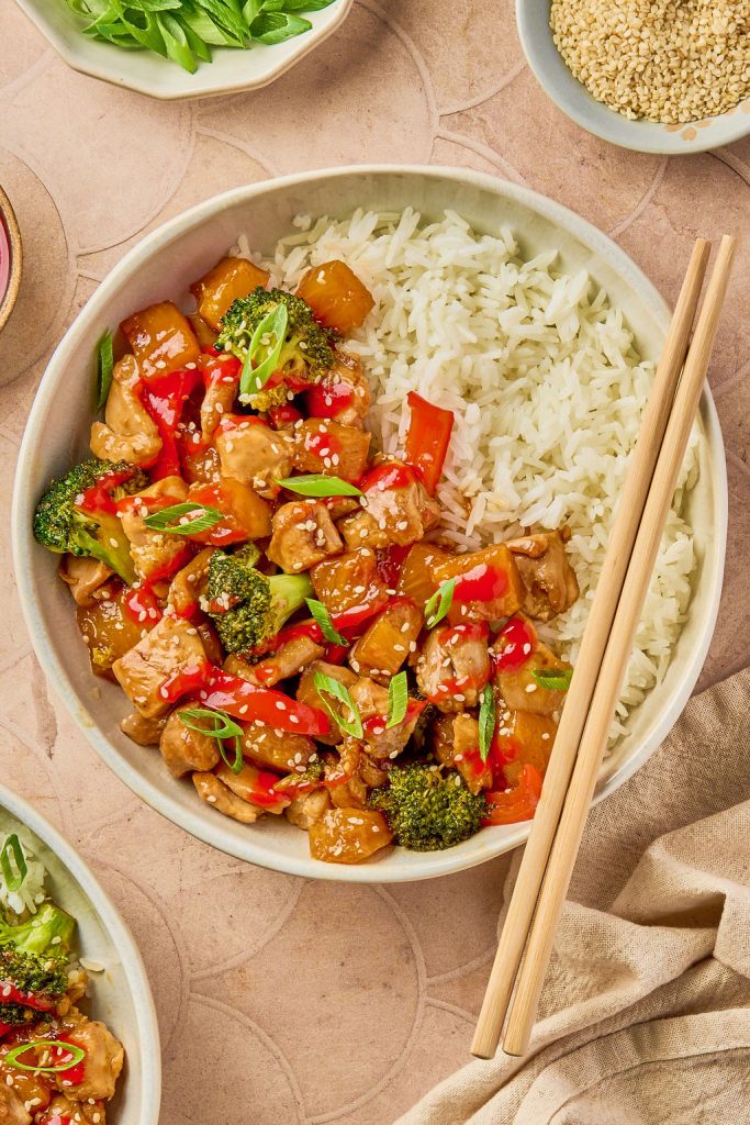 pineapple chicken over white rice in a bowl with chopsticks