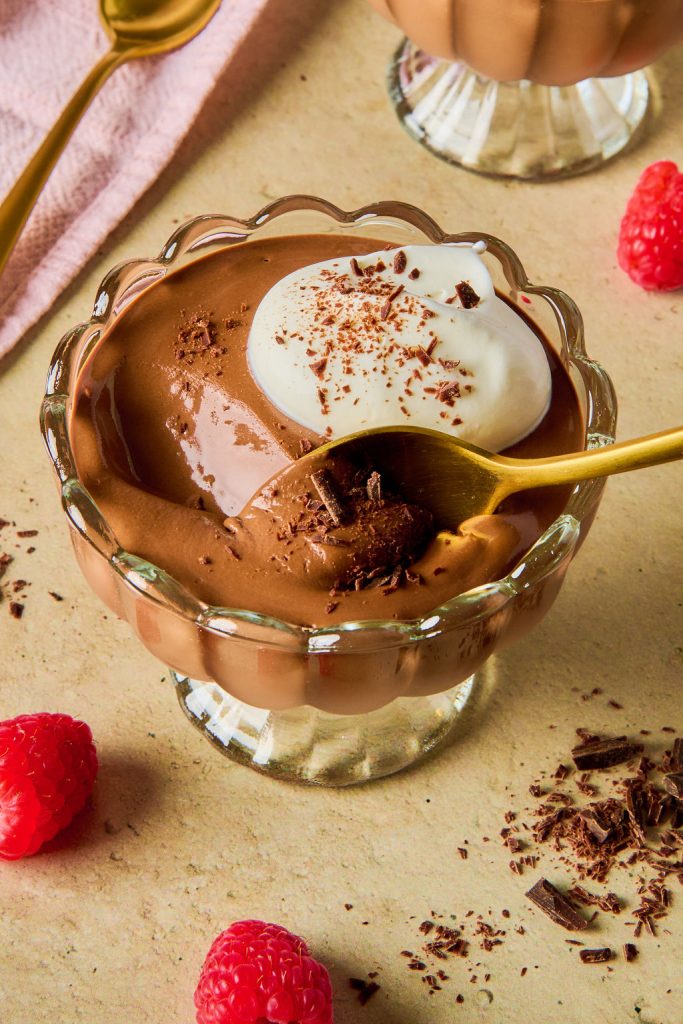 chocolate cottage cheese mousse in a glass bowl with a scoop being taken out by a gold spoon