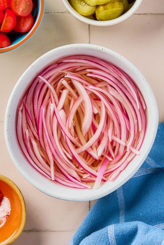 sliced onions in a jar or bowl with vinegar, maple syrup, salt, and hot water