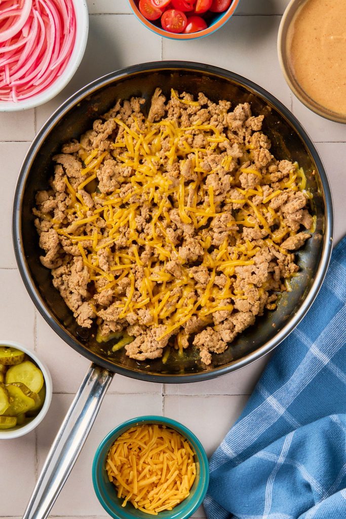 shredded cheese added to cooked meat in skillet