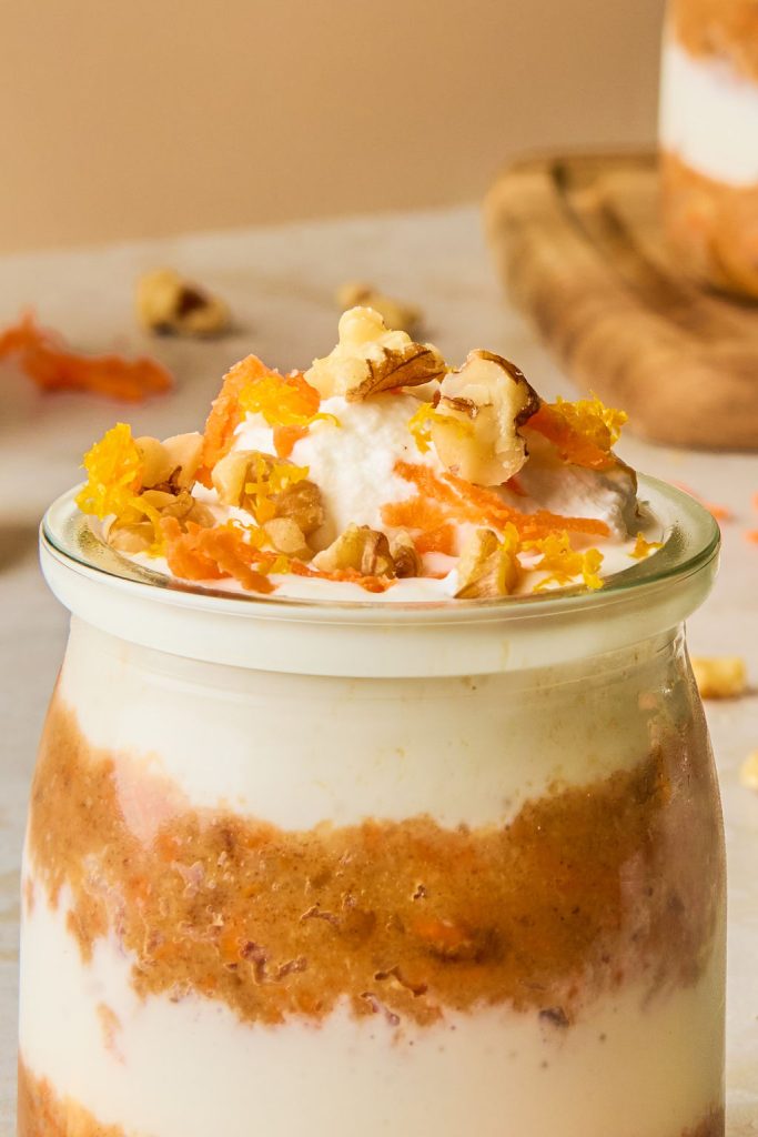 close up of carrot cheesecake jar topped carrot shreds, nuts and whipped cream