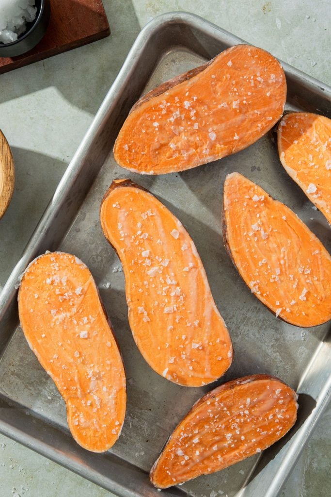 sweet potatoes cut in half on a baking sheet and topped with sea salt