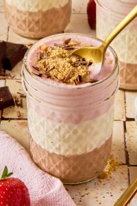 neapolitan cheesecake jar topped with graham crackers and chocolate shavings