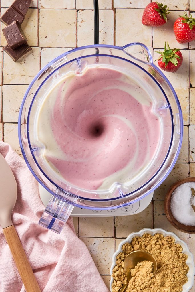 strawberries being blended in a blender with cheesecake base