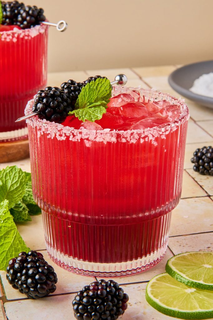 close up of blackberry margarita in a glass topped with blackberries and mint