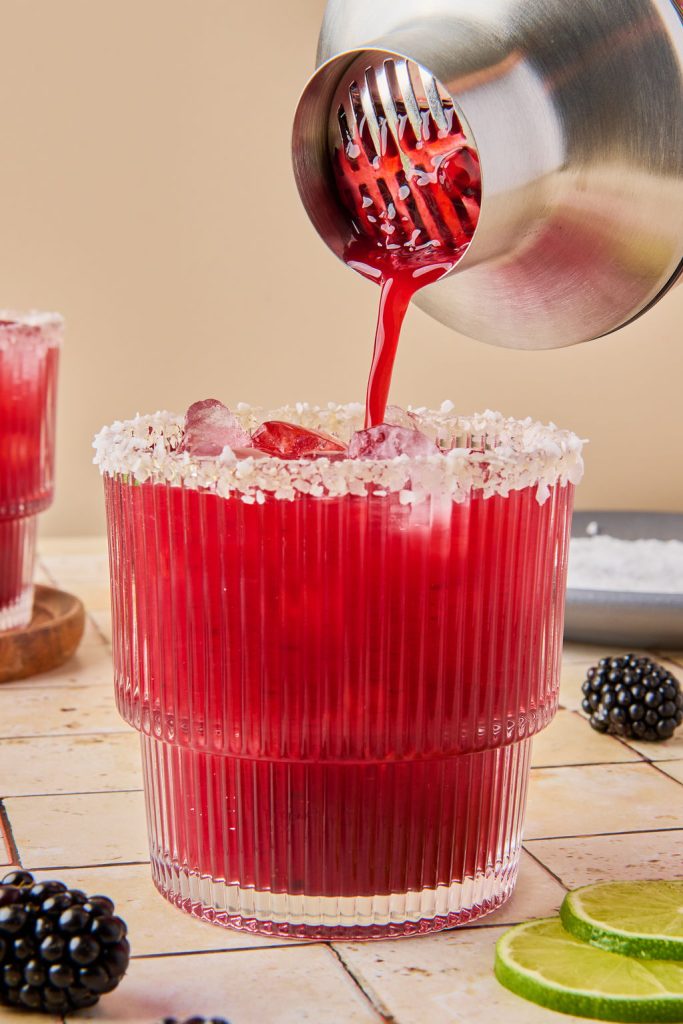 blackberry margarita being poured from a shaker to a glass