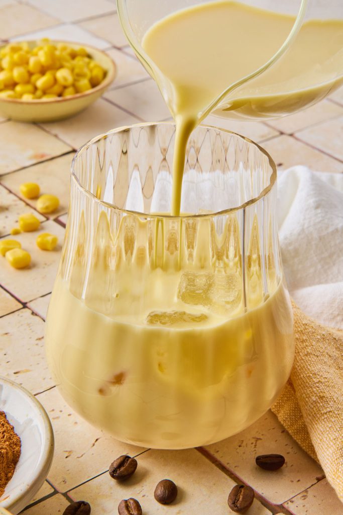 corn milk being poured into a glass with ice