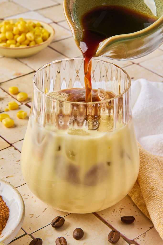 espresso being poured into corn milk in a glass with ice