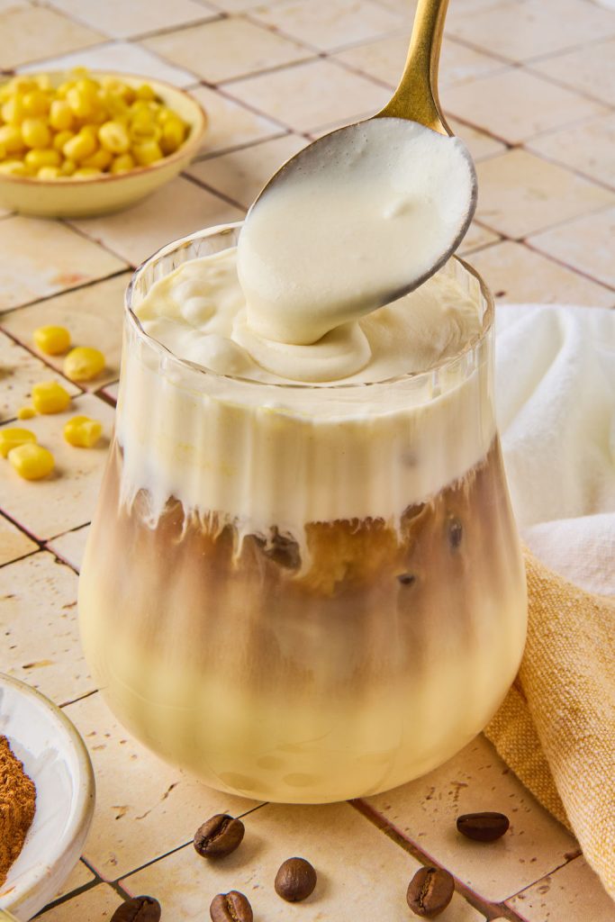 corn cold foam being added to the corn latte in a glass