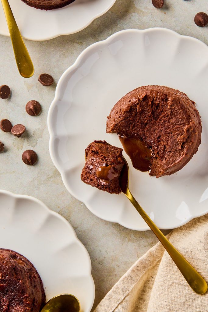 lava cake on a plate with a gold spoon scooping a bite and the chocolate center melting out