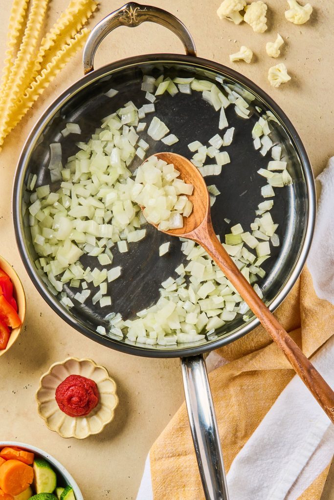 diced onion being cooked in a skillet with a wooden spoon