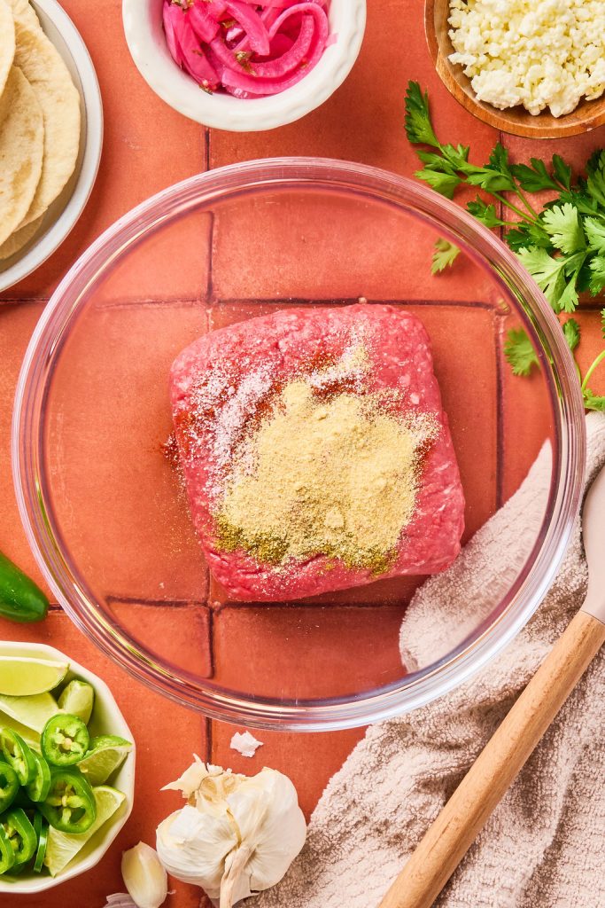 spices added to ground beef in a glass bowl