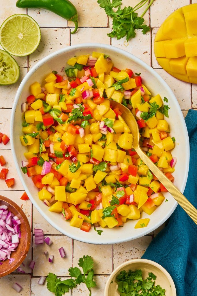 all the mango salsa ingredients mixed together with a gold spoon in a bowl