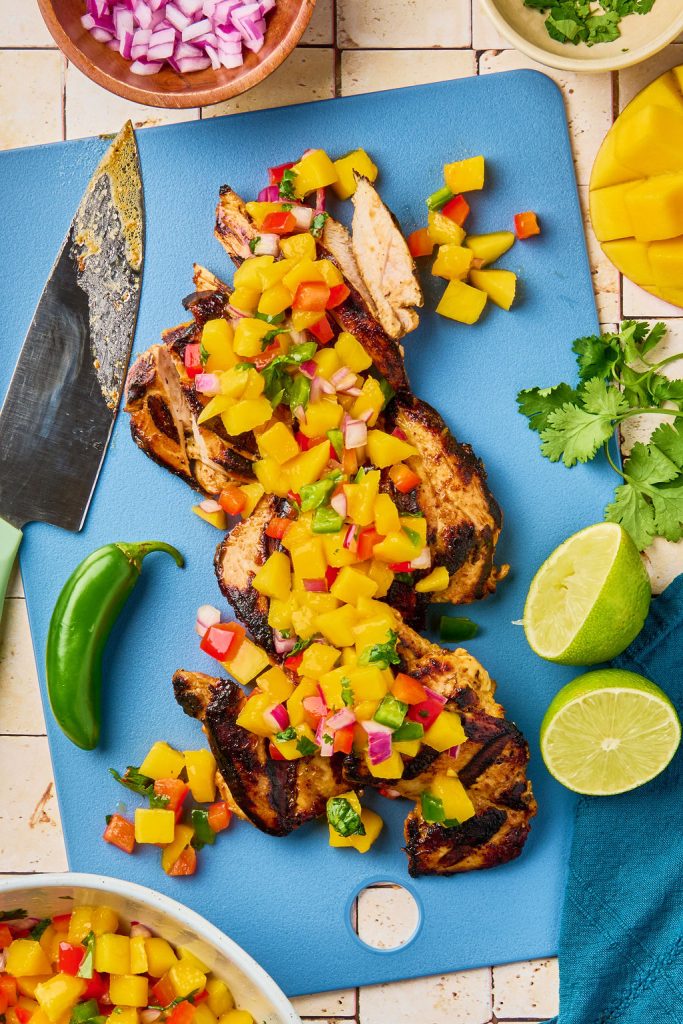 sliced mango chicken on a cutting board topped with mango salsa
