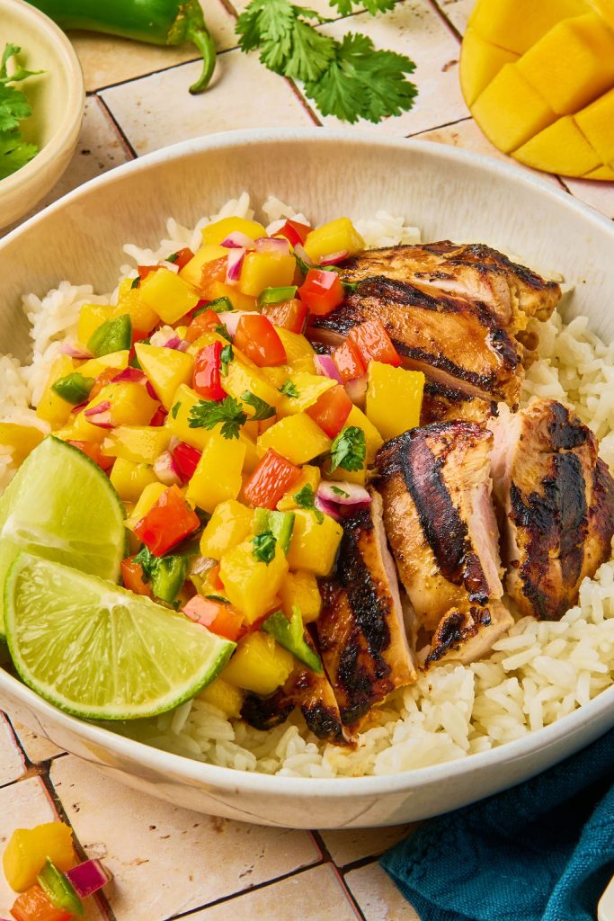 marinated mango chicken sliced on top of rice and topped with mango salsa and lime wedge