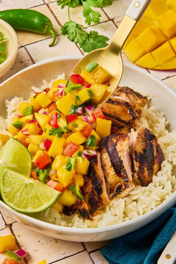 mango chicken on a bed of rice topped with mango salsa and lime wedges