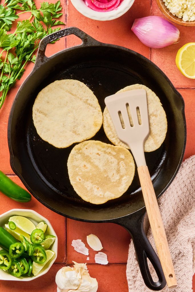tacos being smashed with a spatula in skillet while they cook