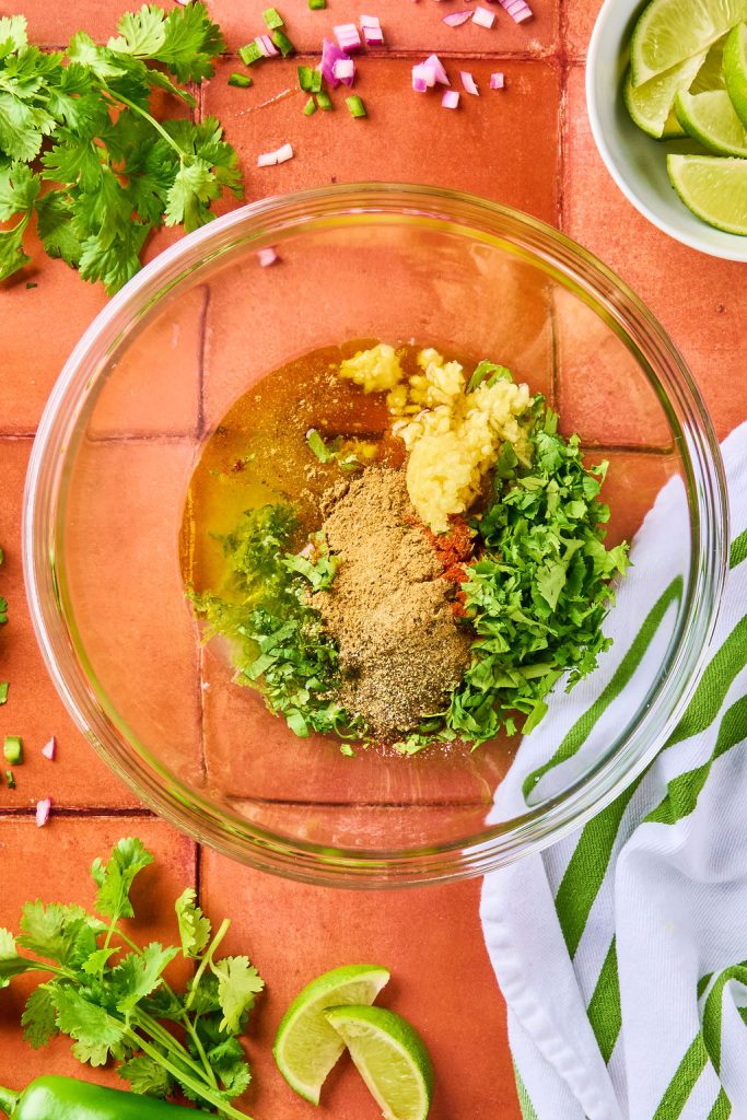 lime juice, lime zest, olive oil, cilantro, garlic, honey, jalapeño, red onion and spices in a glass bowl