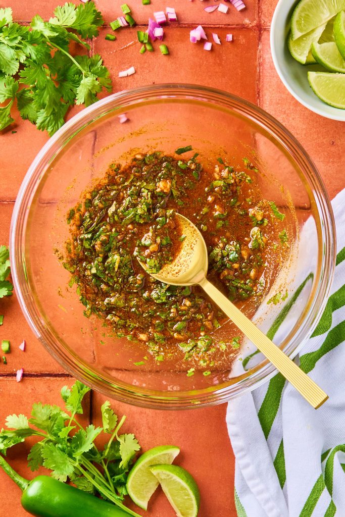 all the marinade spices mixed together in a glass bowl with a gold spoon