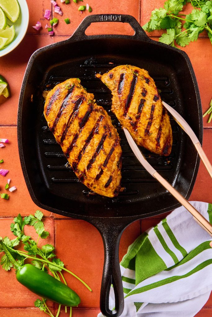 grilled chicken breasts on a skillet being turned over with tongs