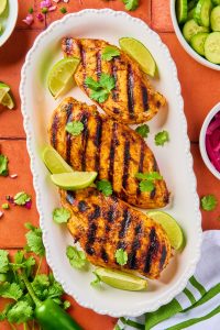 3 cilantro lime chicken marinated breasts on a white platter toped with lime wedges and cilantro