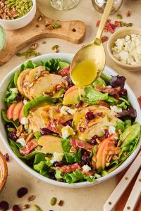 gold spoon drizzling maple dijon dressing over chicken and cranberry salad