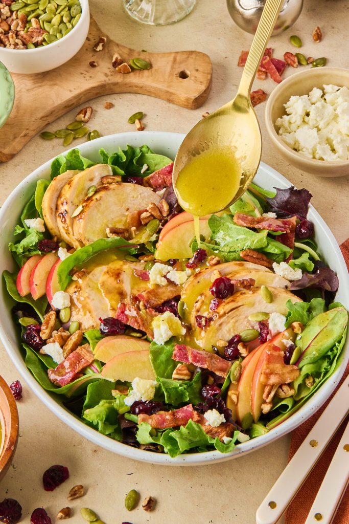 gold spoon drizzling maple dijon dressing over chicken and cranberry salad