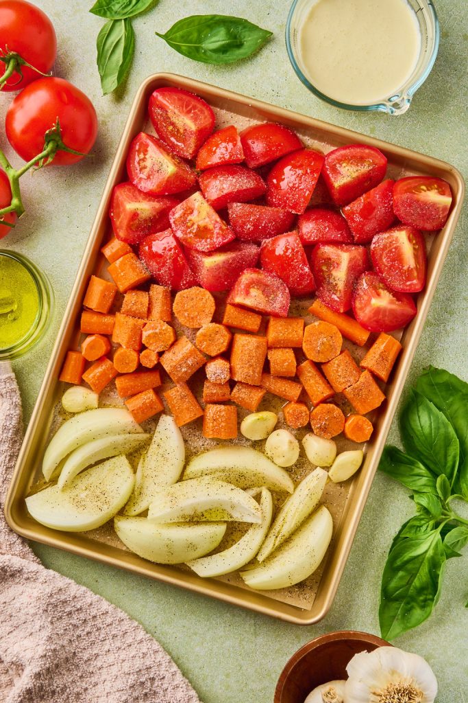 tomatoes, carrots, onion, and garlic cloves in an even layer on a lined sheet pan
