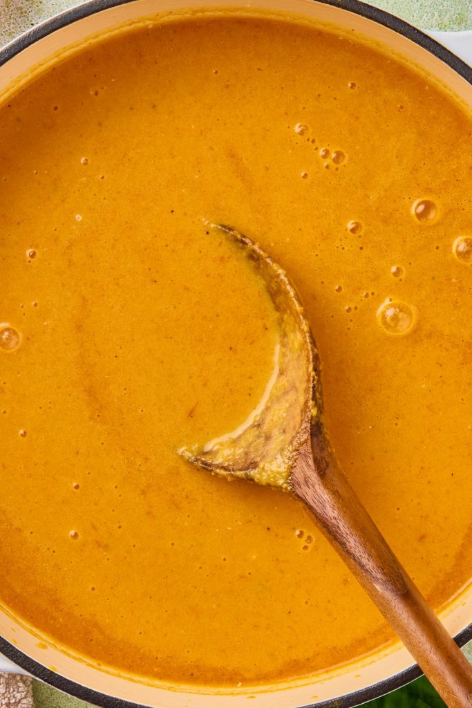 close up of carrot tomato soup being stirred with a wooden spoon