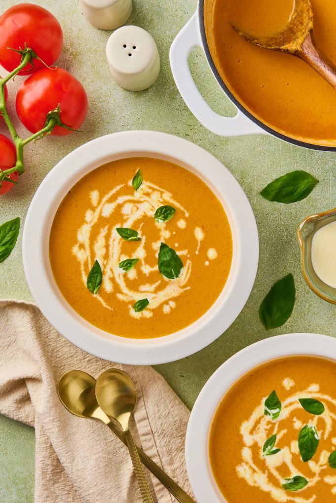 two bowls of carrot tomato soup drizzled with more coconut milk and some basil