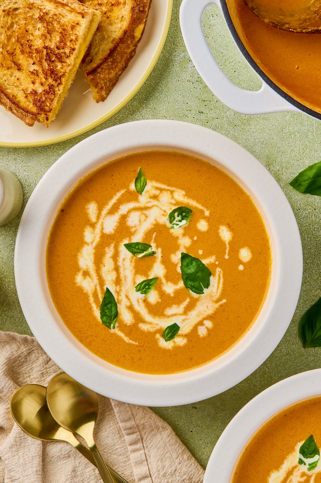 bowl of carrot tomato soup drizzled with more coconut milk and some basil