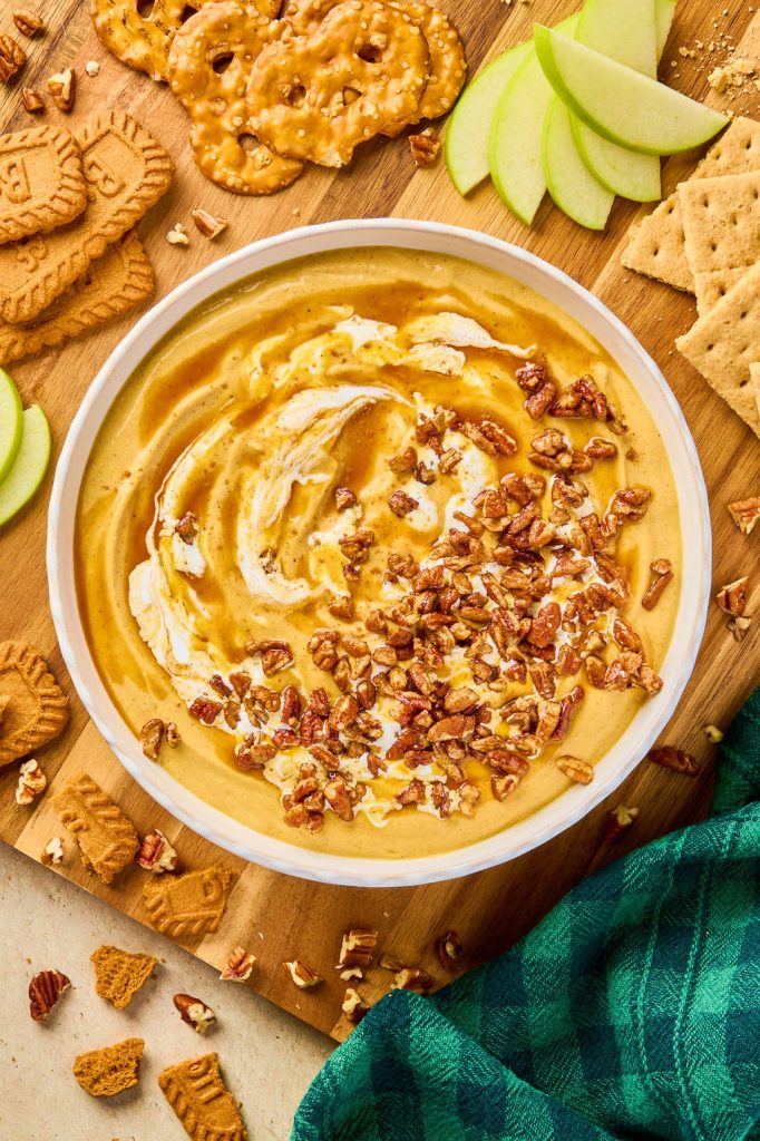 maple pecan pumpkin dip in a bowl surrounded by apples, graham crackers, pretzels, and biscoff cookies