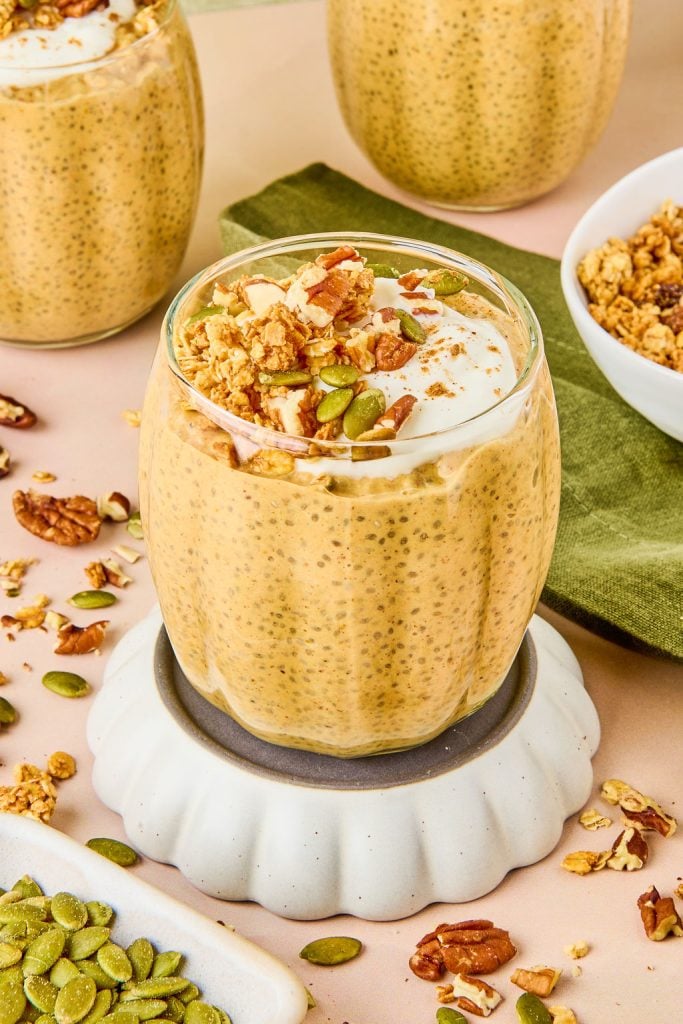 pumpkin pie chia pudding in a glass cup topped with pumpkin seeds and granola and nuts