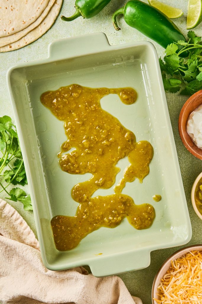 green enchilada sauce on the bottom of a baking dish