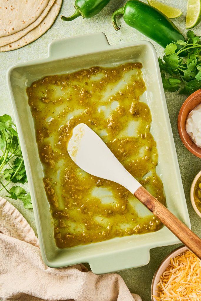 green enchilada sauce spread along the bottom of a baking dish with a spatula