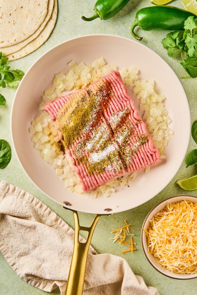ground beef and spices added to diced onions in the skillet