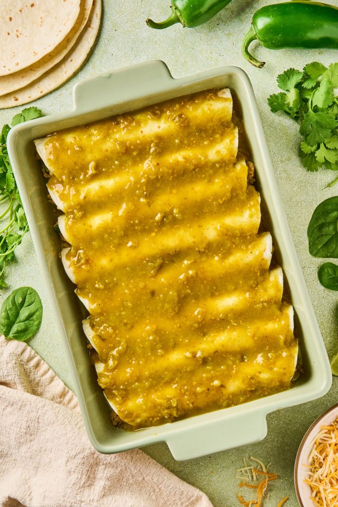 green enchilada sauce poured over enchiladas in the baking dish