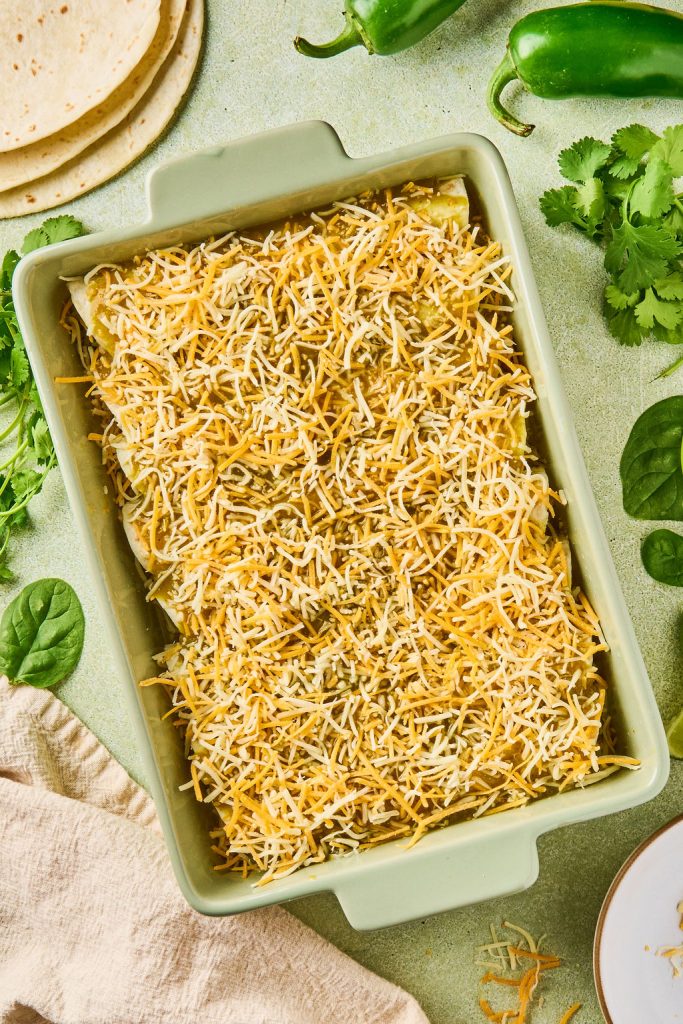 shredded cheese sprinkled over the green sauce enchiladas in the baking dish