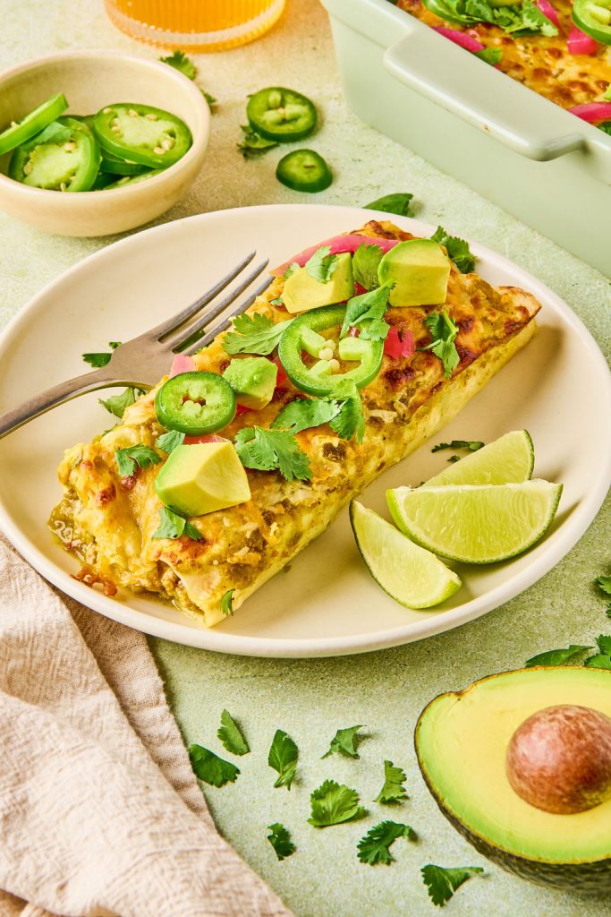 turkey enchiladas plated and topped with pickled onions, avocado cilantro and jalapeños with lime wedges on the side
