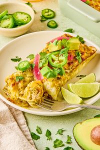 Turkey enchiladas on a plate topped with cilantro, jalapeños, red onion