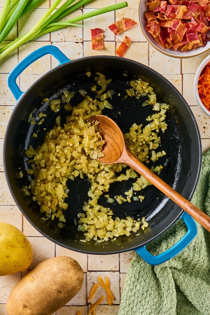 onions cooked down in a pot and being stirred with a wooden spoon