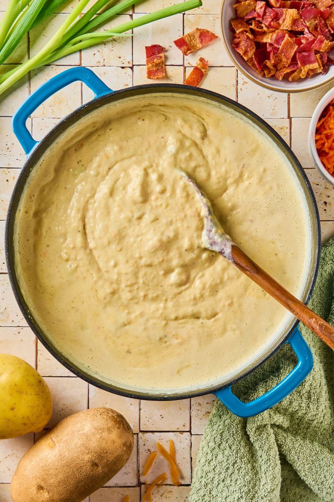 thick creamy potato soup in the pot being stirred with a wooden spoon
